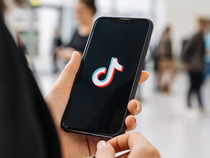 a closeup of a man holding a phone with the tiktok logo splash screen on it