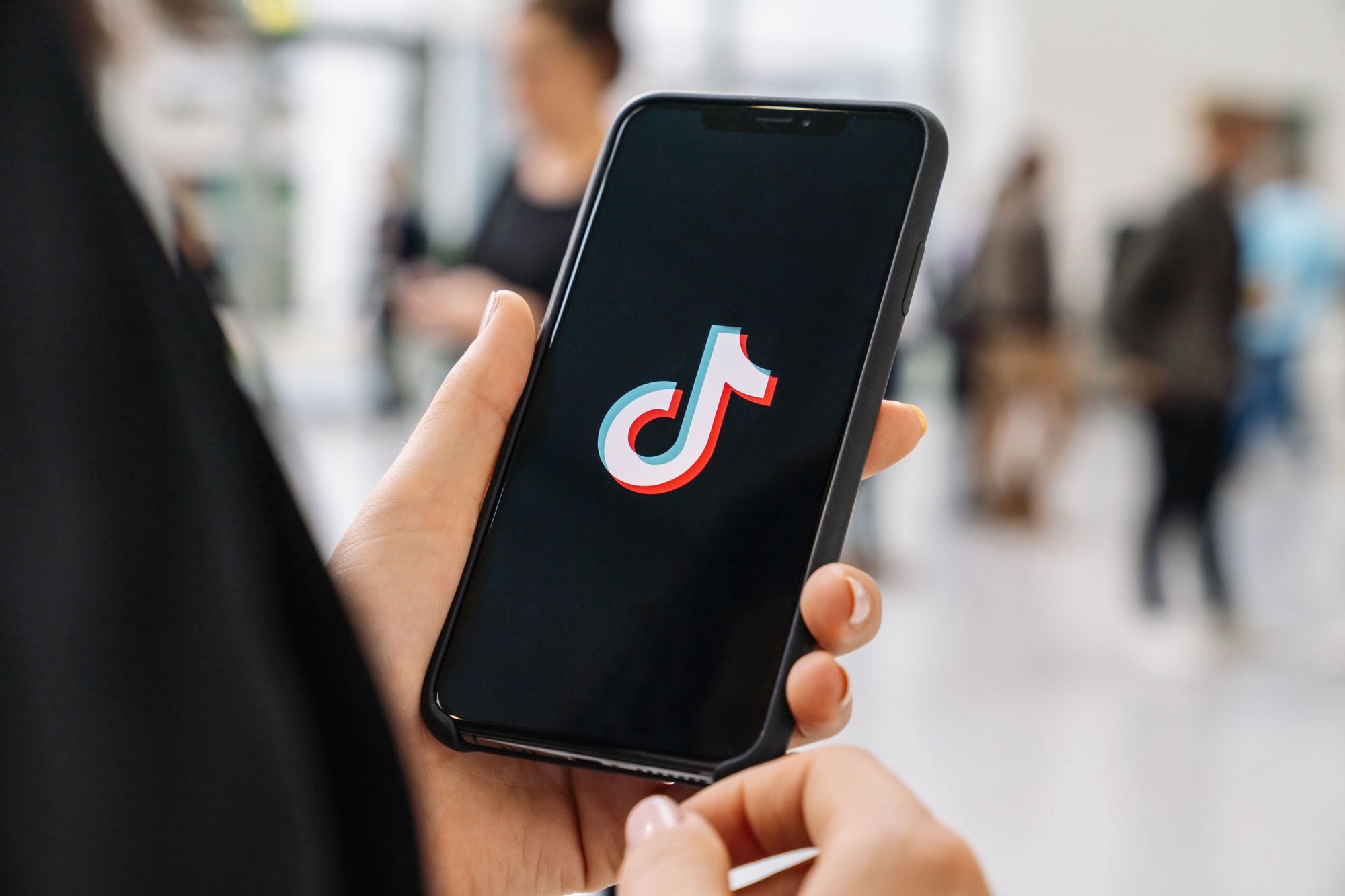 a closeup of a man holding a phone with the tiktok logo splash screen on it